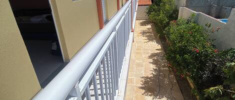 A building with a balcony, a tiled pathway, and a garden area.