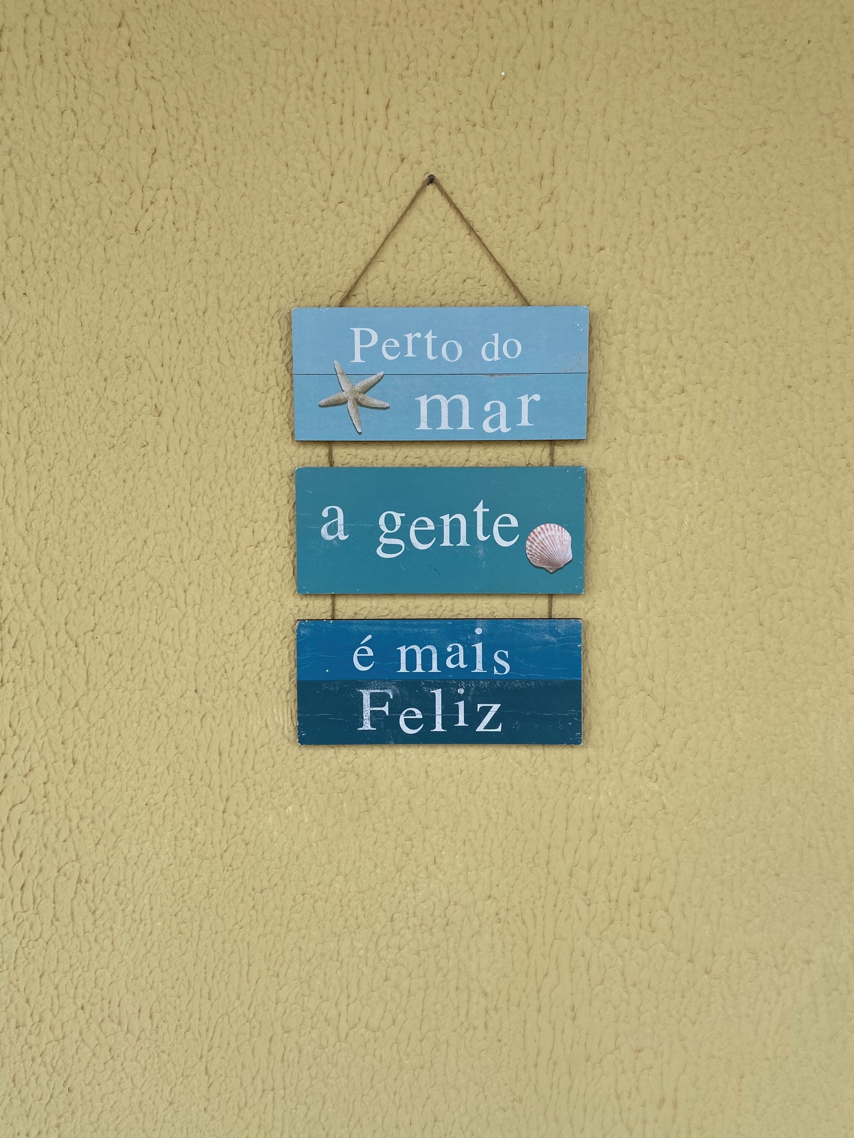 Ein an der Wand befestigtes Schild mit drei blauen Holzfeldern, jeweils mit weißer Schrift und einer Meerfabel-Dekoration.