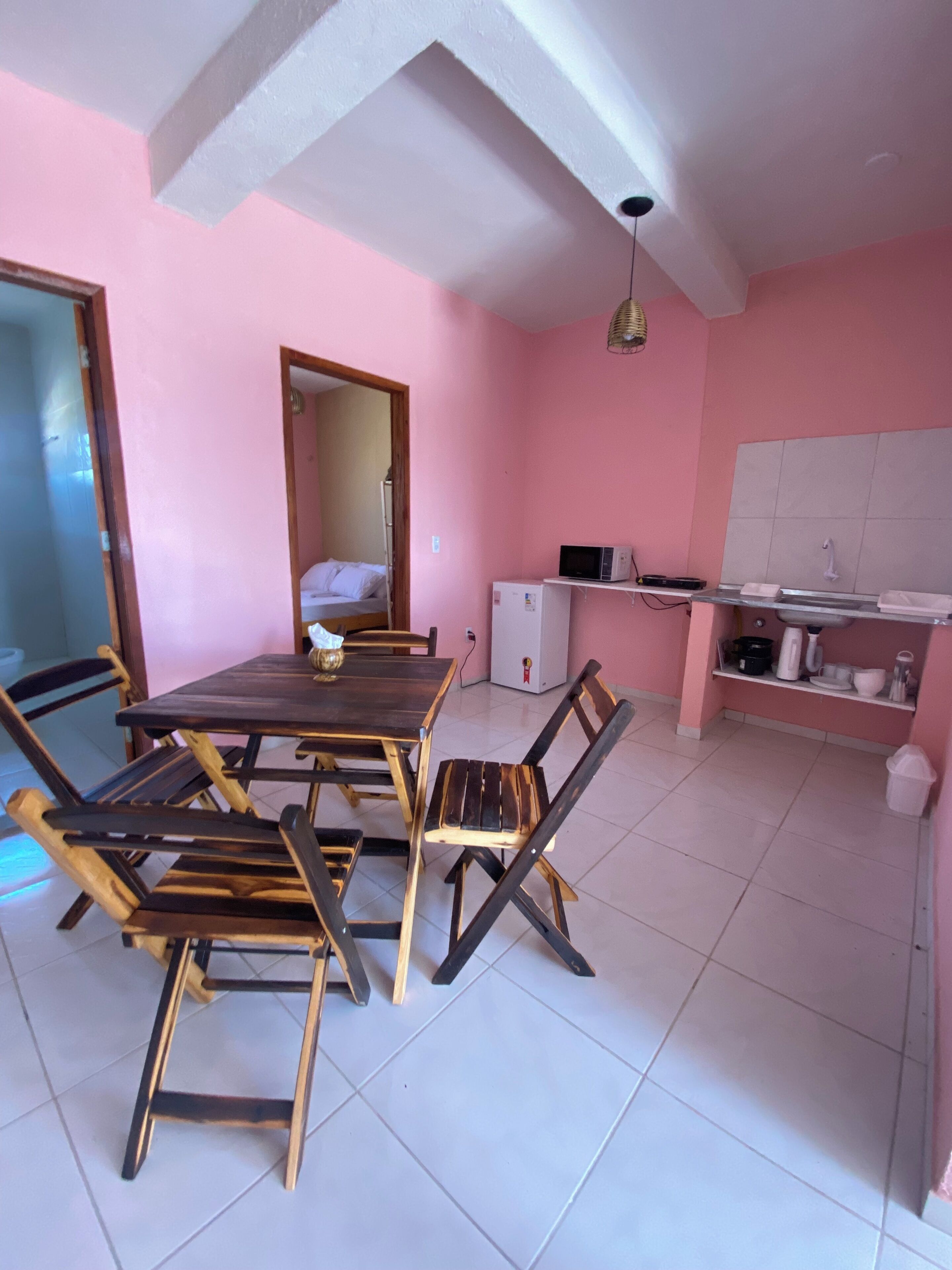 A dining area with a wooden table and chairs, a kitchen with a microwave and sink, and a mirror on the wall.
