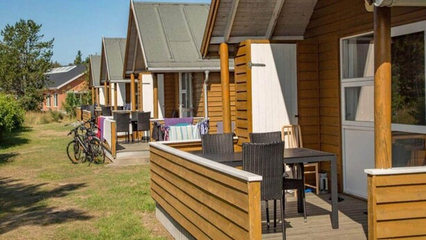 A row of wooden cabins with outdoor seating areas, bicycles, and a grassy yard.