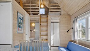 A cabin interior with a dining table, chairs, a sofa, a small window, and a door.