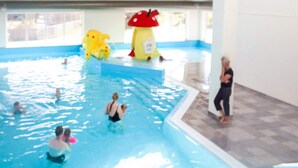 An indoor swimming pool with a blue and white color scheme, a large inflatable character, and a tiled floor around the pool area.