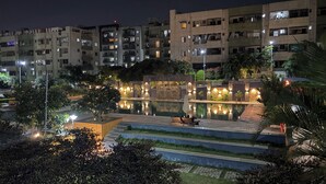 A nighttime view of a residential area with a swimming pool, surrounded by well-lit buildings and lush greenery.