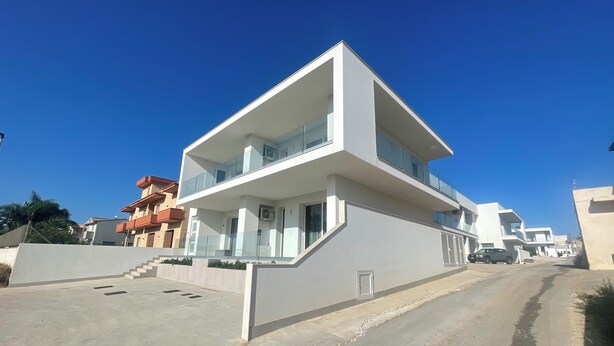A modern two-story building with a flat roof, large windows, and a balcony.