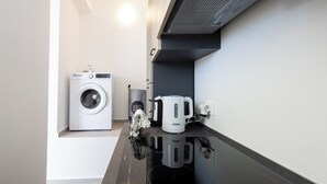A compact kitchen with a washing machine, a kettle, and a coffee maker.