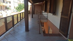 Un balcon doté d’un sol carrelé, de balustrades en bois et offrant une vue sur les bâtiments voisins.