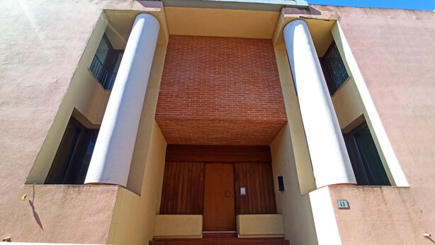 Une entrée d’immeuble avec une porte en bois, deux colonnes et un mur en briques.