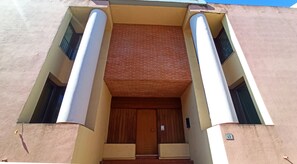 A building entrance with a wooden door, two columns, and a brick wall.