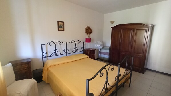 A bedroom with a bed, a wardrobe, a bedside table, a lamp, and a fan.