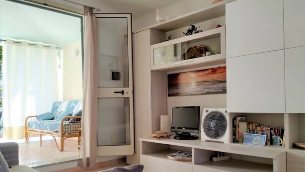 Een woonkamer met een bank, een televisie, een ventilator en een boekenkast.