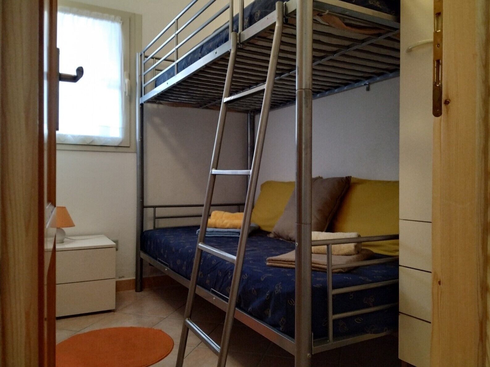 A bunk bed room with a ladder, a small bedside table, and a window.