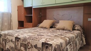 Een slaapkamer met een bed, twee kussens, een hartvormige decoratie op het hoofdeinde en een kledingkast.
