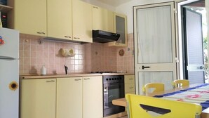 Een keuken met gele kastjes, een fornuis, oven en een eettafel met stoelen.