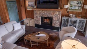 Un salon chaleureux avec une cheminée en pierre, un téléviseur fixé au-dessus, et un coin salon confortable avec un canapé et des fauteuils.