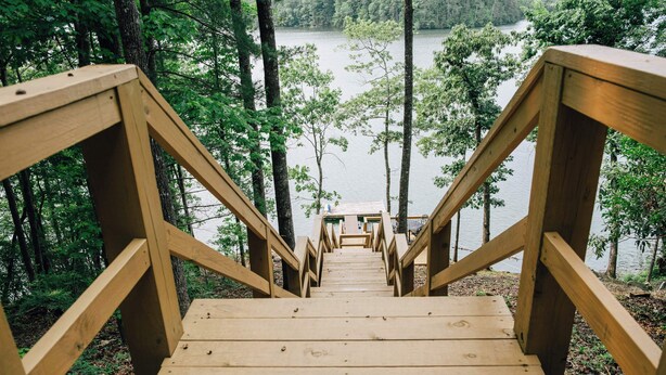 Un escalier en bois mène à une jetée qui surplombe un lac entouré d’arbres.