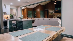 Une cuisine moderne avec des meubles de couleur vert foncé, un îlot central en bois et un coin repas comprenant une table en bois et des sets de table verts.