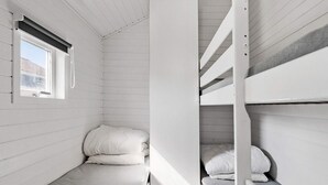 Uma cabana compacta, com um quarto único, uma cama beliche e uma pequena janela.