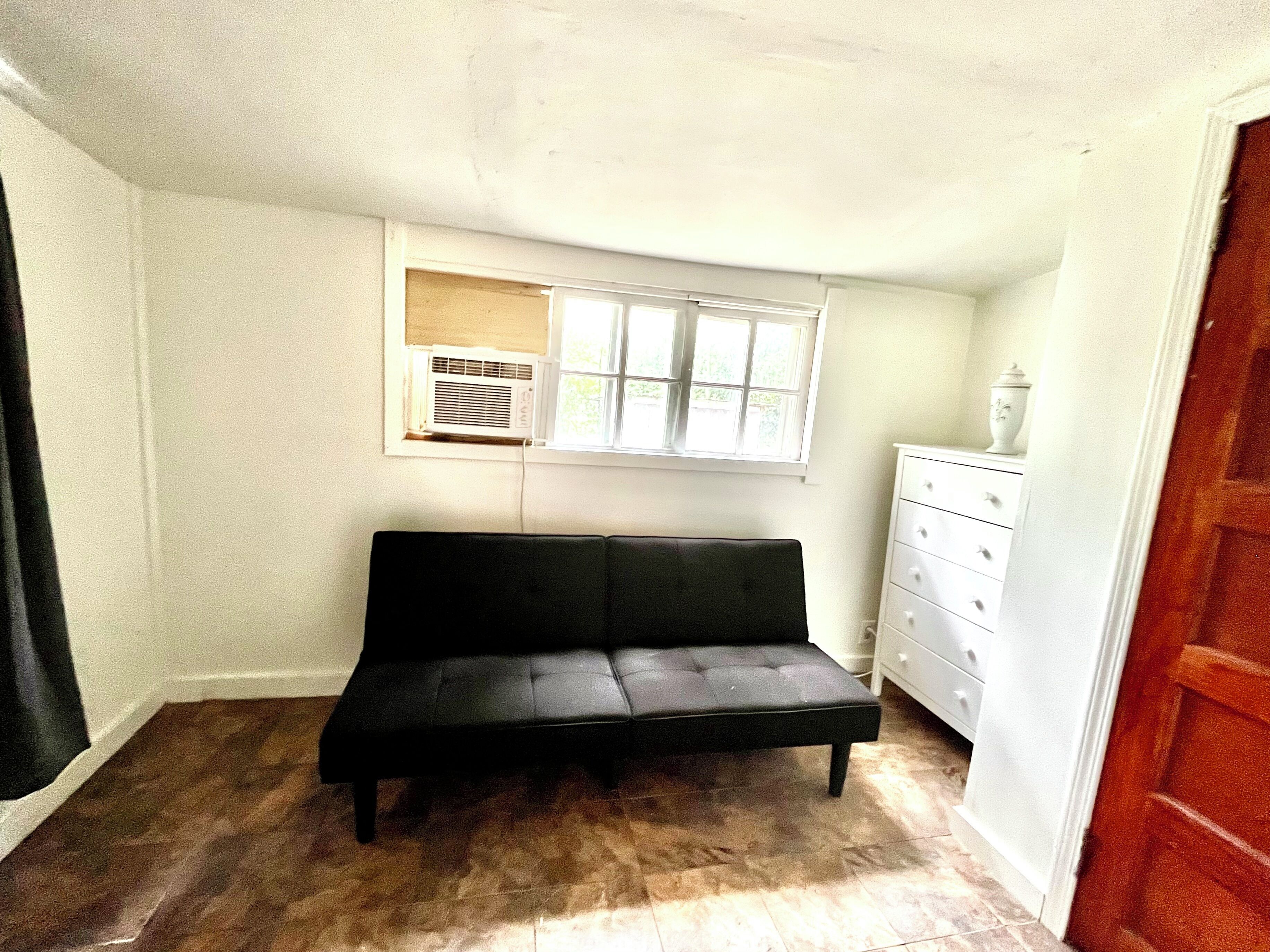 A small room with a black sofa, a white dresser, and a window with blinds.