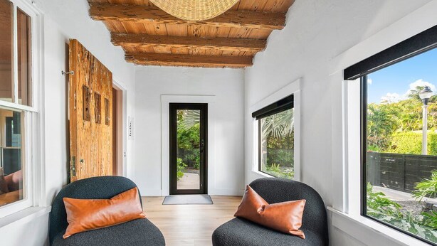 A room with two black chairs, a wooden door, and a large window with a view of greenery. - Hacienda Flamingo Unit 1 - Spacious Designer Flat with Sunroom & Style (West Palm Beach)