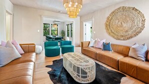 Un salon moderne avec un canapé en cuir marron, des fauteuils turquoise, une table basse en fibres tressées et une grande œuvre d’art murale en fibres tressées.