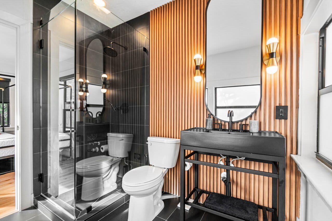 A modern bathroom with a glass shower enclosure, a white toilet, and a black sink with a wooden vanity.