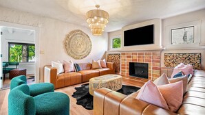 Un salon moderne avec un canapé en cuir, des fauteuils turquoise, une cheminée et une grande œuvre d’art murale.