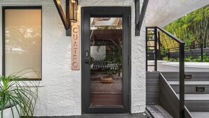 A modern building entrance with a glass door, a sign reading "CUATRO", and a staircase leading to an outdoor area with bamboo plants.