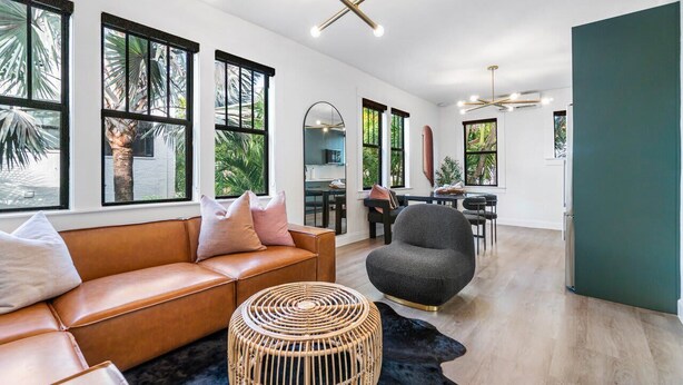 A modern living room with a leather sofa, a round wicker ottoman, and a gray armchair.