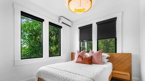 A bedroom with a bed, large windows, and an air conditioning unit.