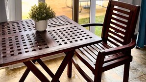A patio area with a table and chair, a potted plant, and a view of a swimming pool and outdoor furniture.