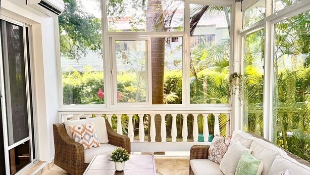 A covered patio with wicker furniture, a wooden table, and a ceiling fan.