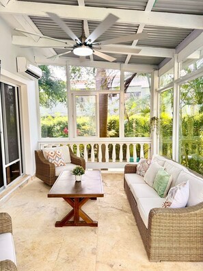 A covered patio with wicker furniture, a wooden table, and a ceiling fan.