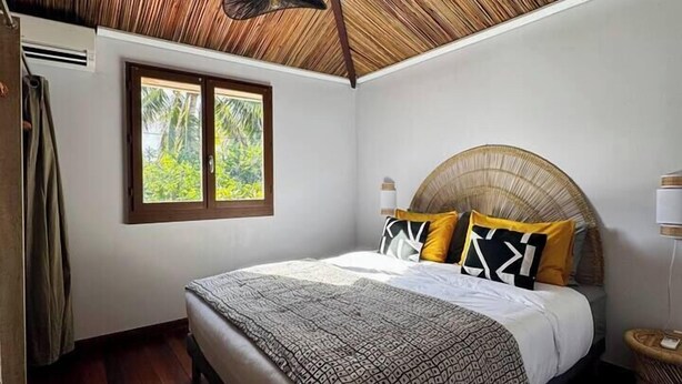 A bedroom with a wooden ceiling, a bed with patterned bedding, and a window with a view of greenery. - Charming Creole house - Private access to the beach (L'Étang-Salé)