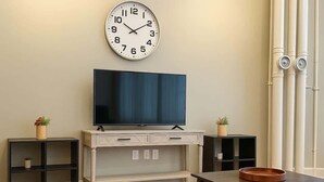 A living room with a flat-screen TV on a white cabinet, a clock on the wall, and a coffee table with a tray. - King Bed Studio Loft. Huge Beautiful Ceilings (Dallas)