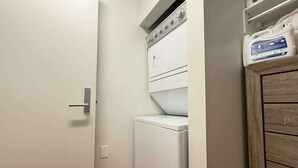 A laundry room with a white washing machine and dryer, a wooden cabinet, and a shelf with cleaning supplies. - King Bed Studio Loft. Huge Beautiful Ceilings (Dallas)