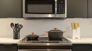 A kitchen with a stainless steel microwave, stove, and oven. There are pots on the stove and a utensil holder on the counter. - King Bed Studio Loft. Huge Beautiful Ceilings (Dallas)
