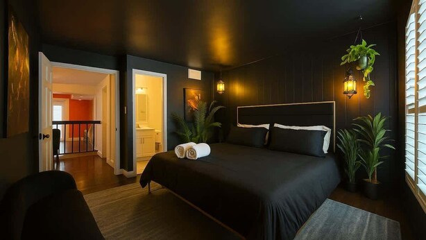 A modern bedroom with a large bed, bedside lamps, and potted plants.