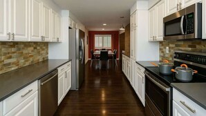 A modern kitchen with white cabinets, stainless steel appliances, and a dark wood floor.