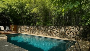 A swimming pool with a stone wall and a wooden deck with chairs.
