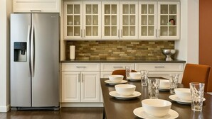 A modern kitchen with white cabinetry, a stainless steel refrigerator, and a dining table set with bowls and glasses.