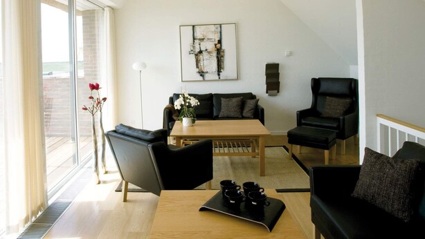 Una sala de estar moderna con techos altos, una mesa de comedor con sillas, un sofá y una mesa de centro con tazas.