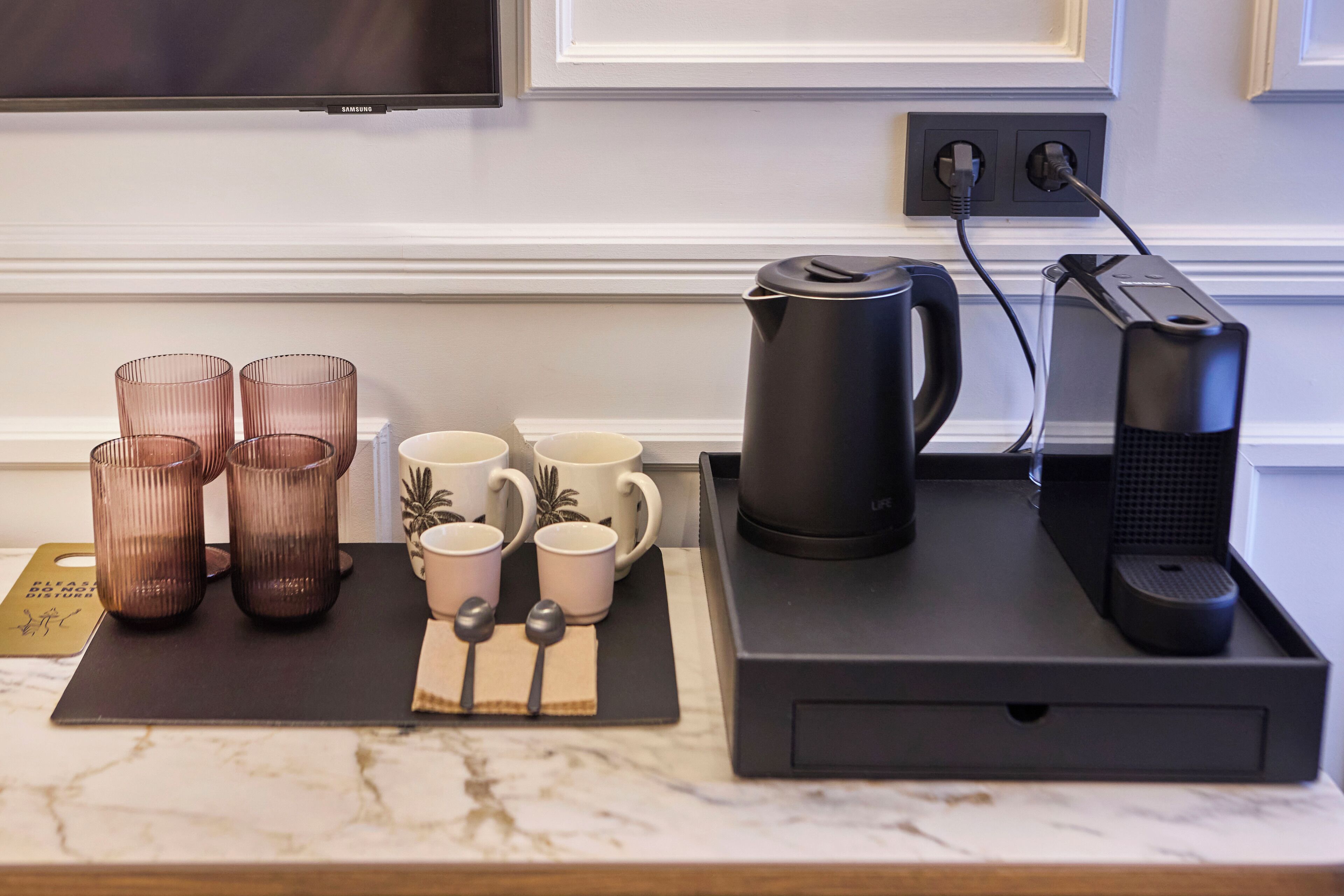 Una encimera de cocina con una cafetera, un hervidor y cuatro tazas.
