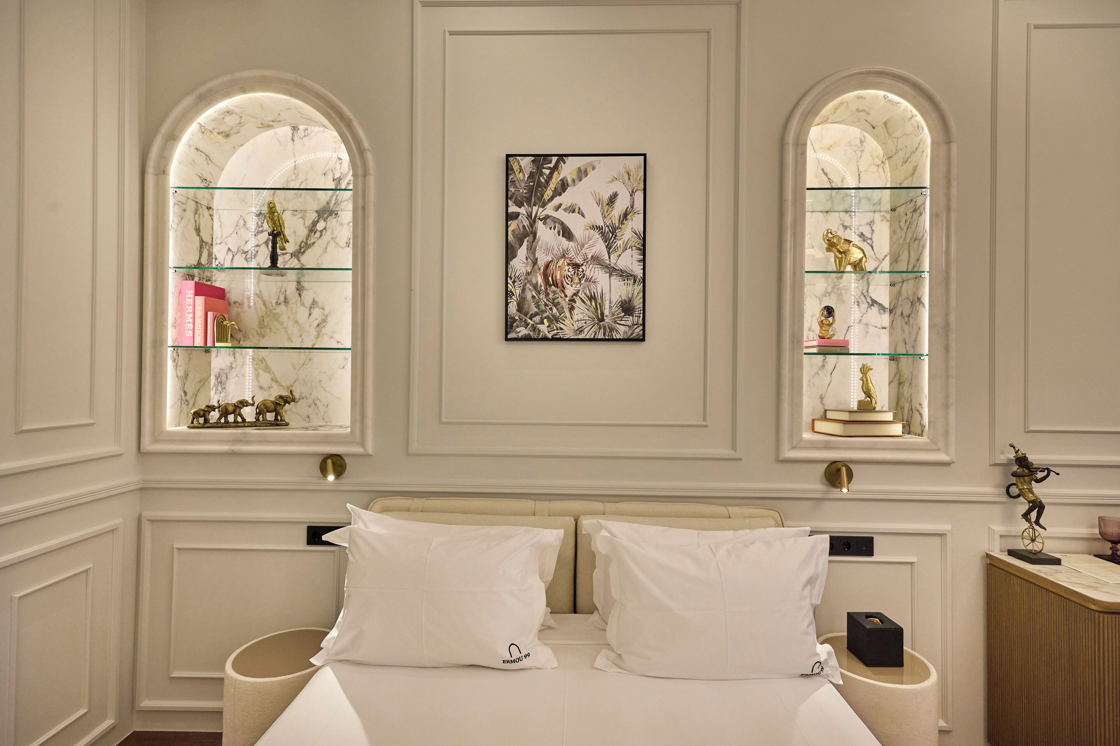 A hotel room with a large bed, two bedside tables, a wall-mounted artwork, and shelves with decorative items.