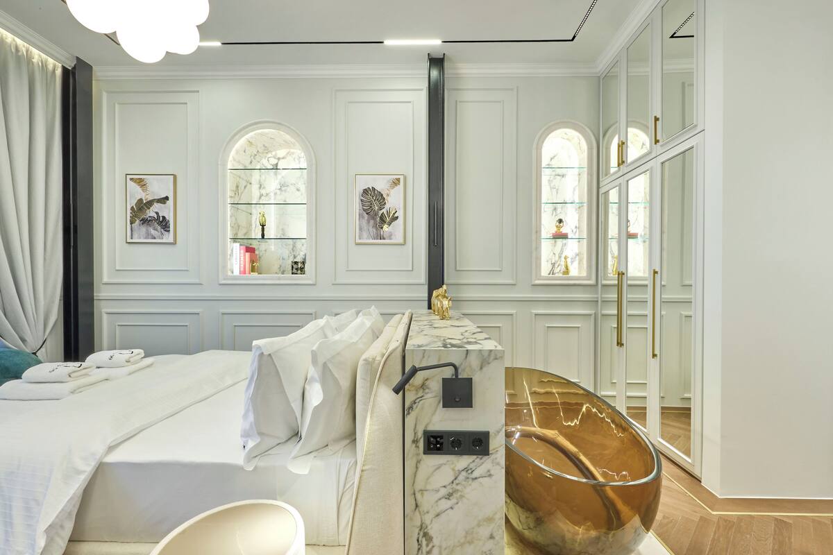 A modern hotel room with a bed, a marble bedside table, a large mirror, and a decorative bowl.