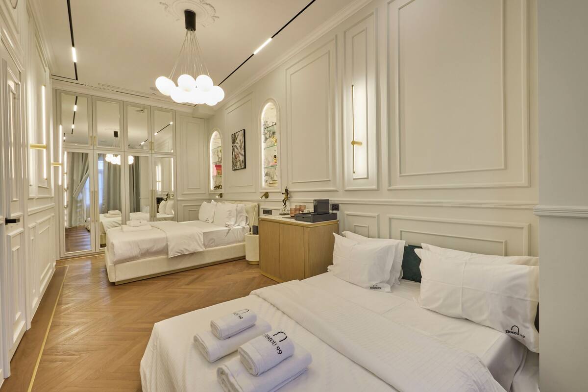 A hotel room with a large bed, a smaller bed, a vanity with a mirror, and a desk with a lamp.