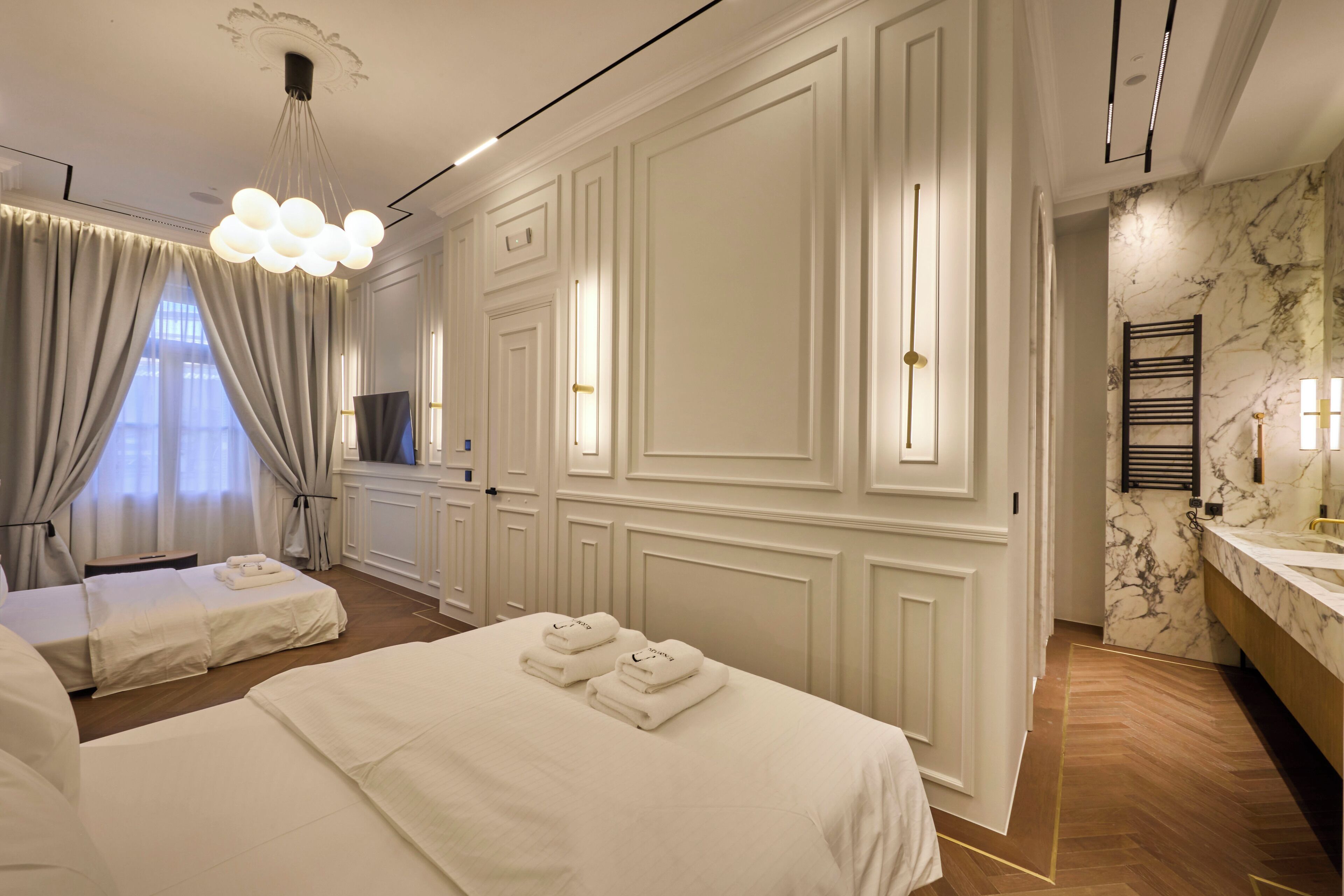 Ein Hotelzimmer mit zwei Betten, einem großen Spiegel, einem Badezimmer mit Marmor und einer Kristallleuchtre.