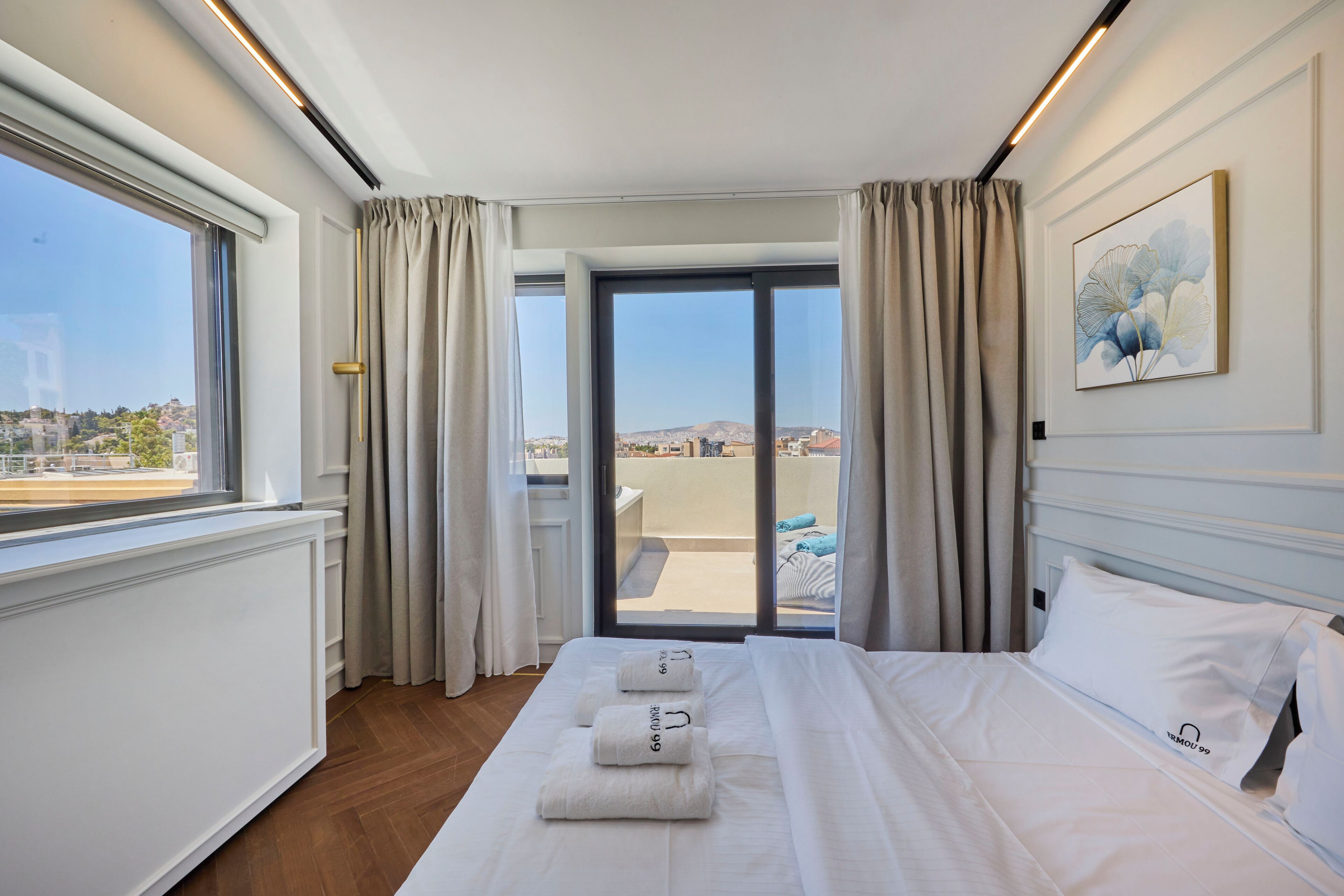A hotel room with a bed, a view of the city, and a painting on the wall.