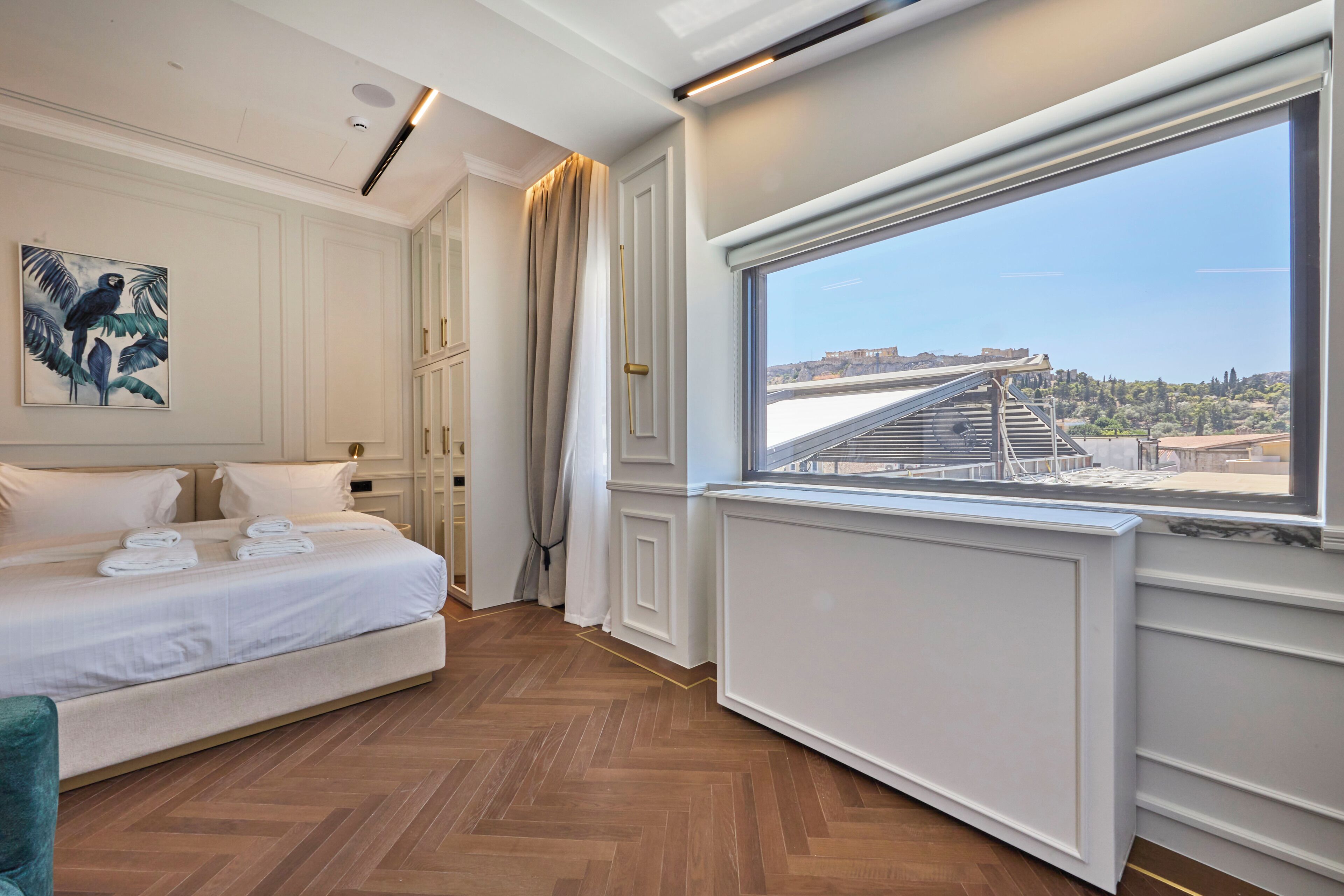 A hotel room with a bed, a window with a view of a cityscape, and a painting on the wall.