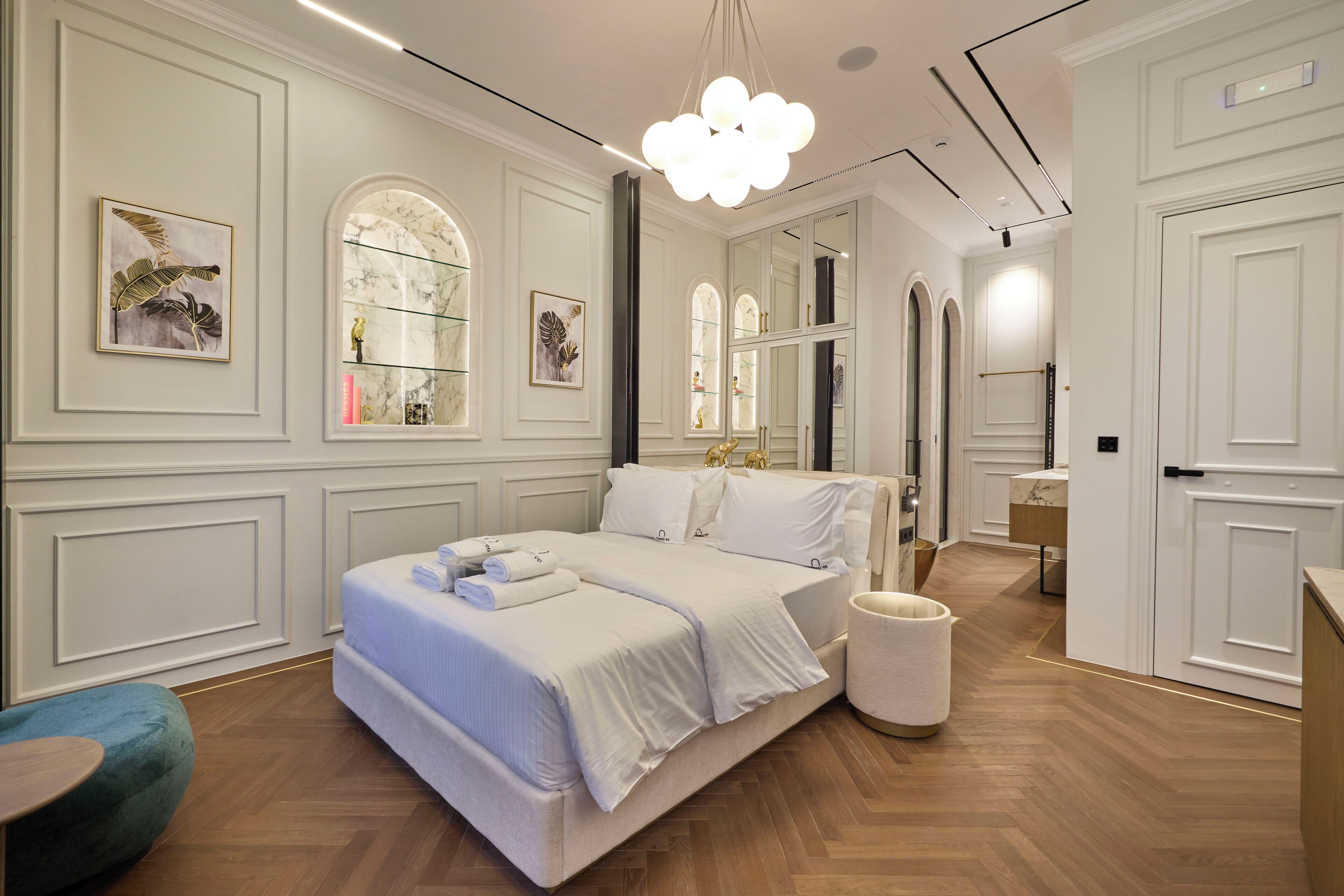 A modern hotel room with a large bed, a vanity with a mirror, and a chandelier.