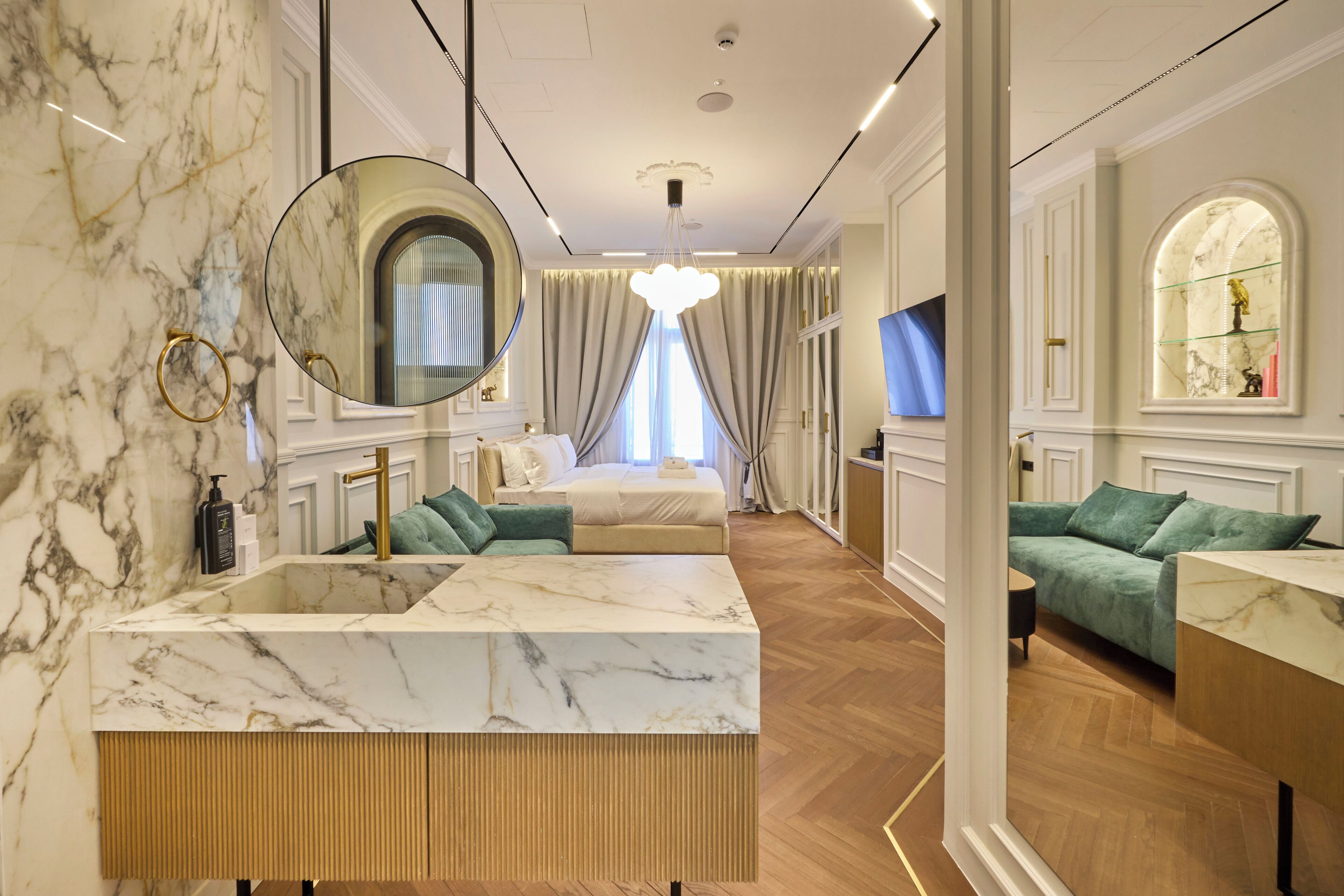 A luxurious hotel room with a marble bathroom, a large bed, a green sofa, and a TV.